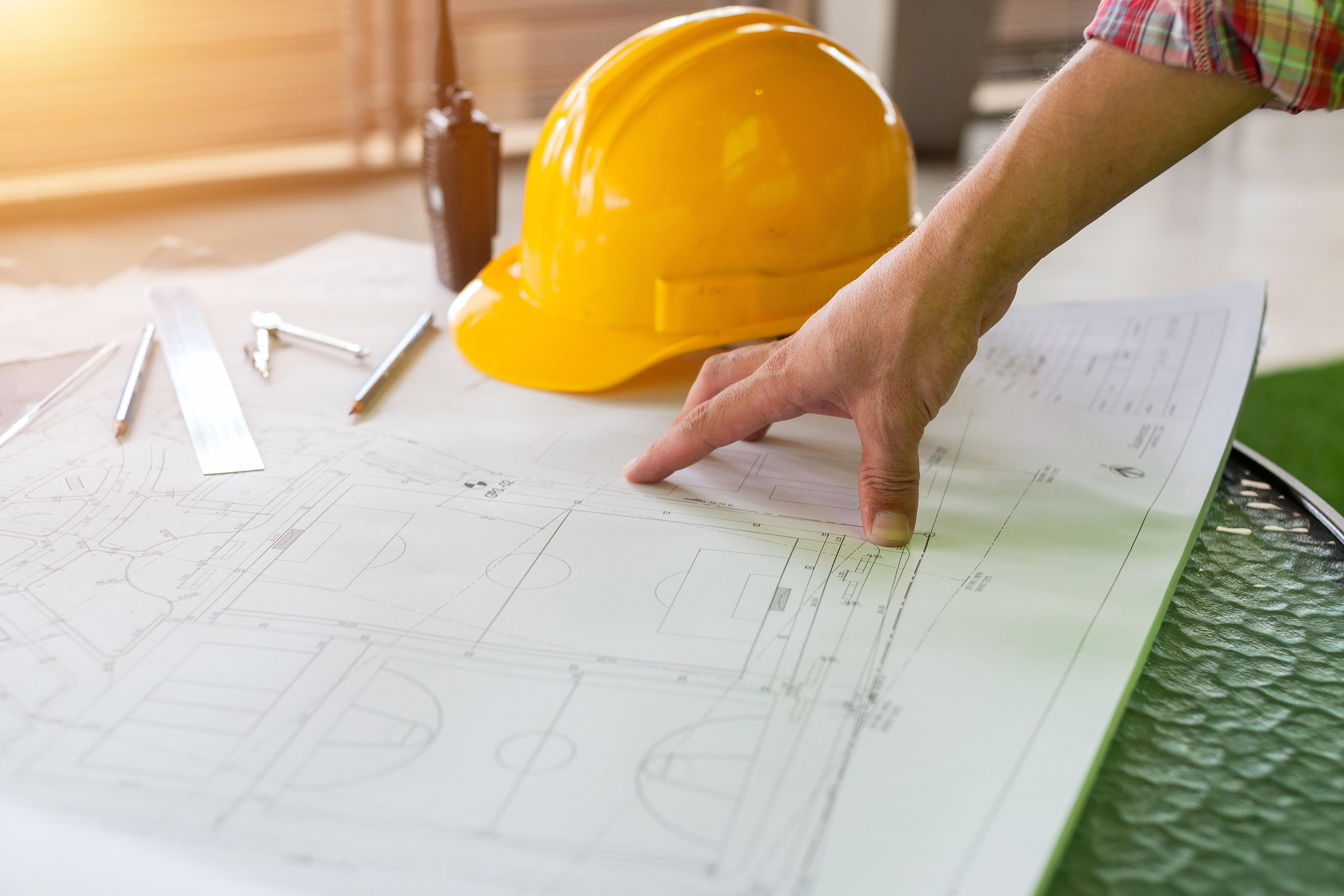 A contractor looking at blueprints with a yellow hardhat on the table.