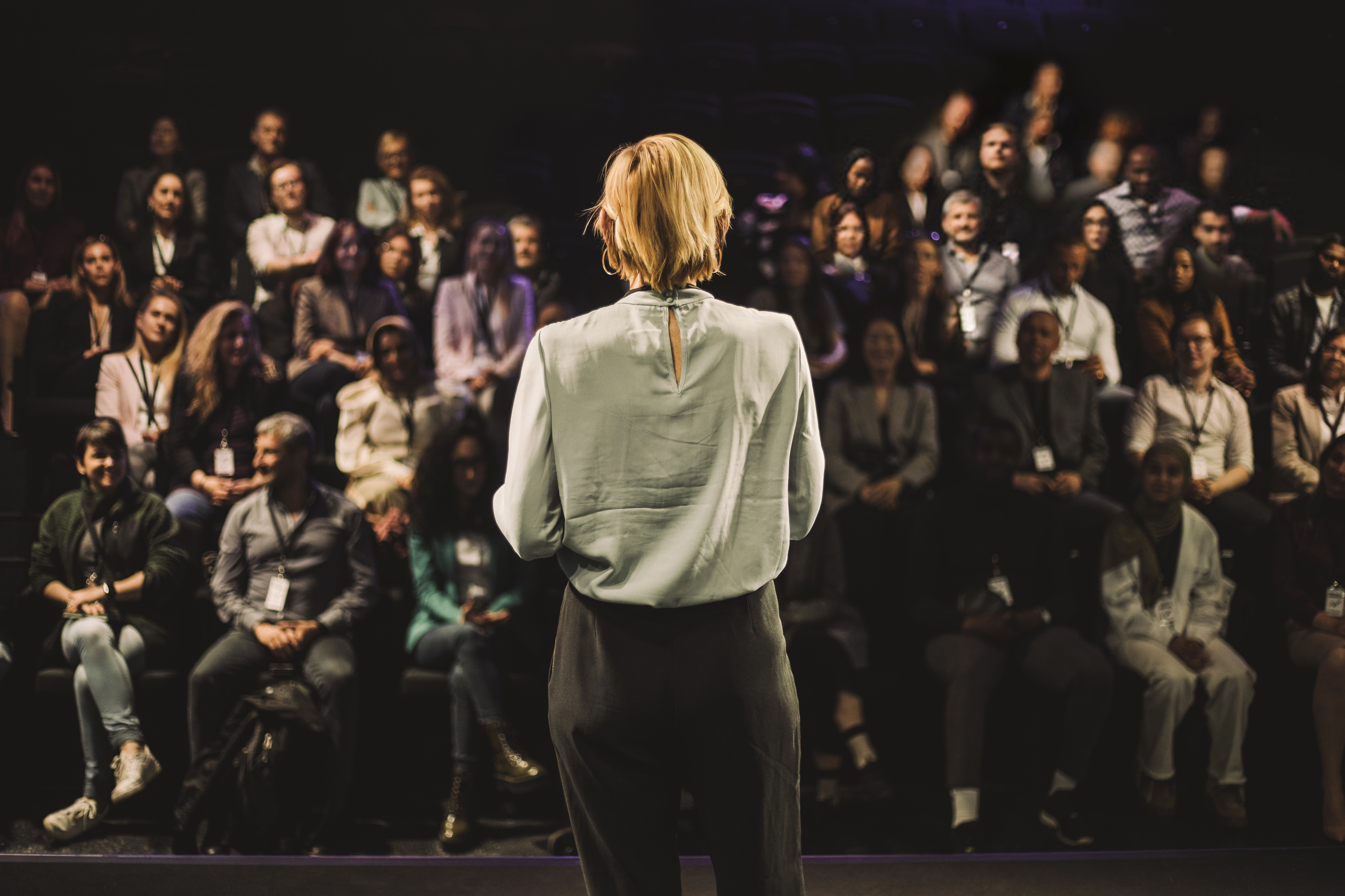 Blonde woman speaking to a large group at a conference
