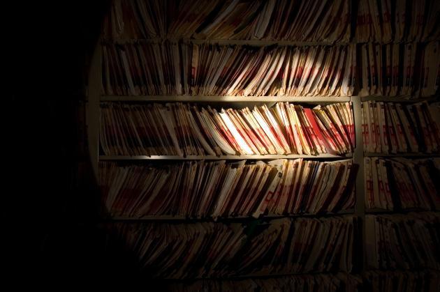 A bookshelf in the dark, with a section illuminated by a flashlight off-screen.